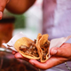 A hand holding two carnitas street tacos in corn tortillas